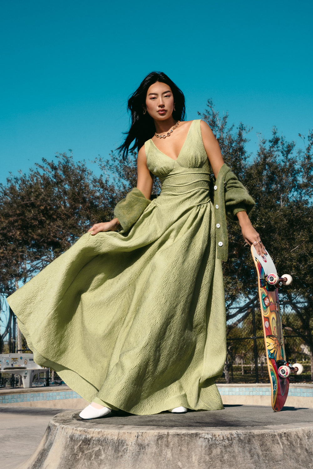 a woman in a long green dress holding a skateboard